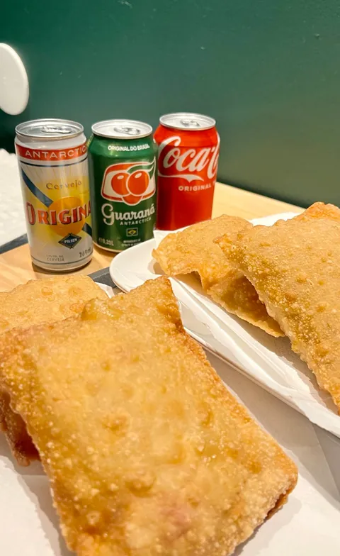 Kultaisiksi paistettuja pastel-taskuja lautasella, taustalla Guaraná Antarctica-, Antarctica Original- ja Coca-Cola-tölkit.